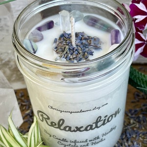 May include: A white soy candle in a clear glass jar with a white label that reads "Relaxation Soy Candle infused with Healing Crystals and Herbs". The candle is topped with dried lavender and clear crystals.