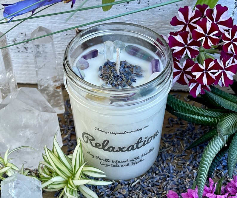 May include: A white soy candle in a clear glass jar with a label that reads "Relaxation Soy Candle infused with Healing Crystals and Herbs" and a decorative top with lavender buds and clear crystals.