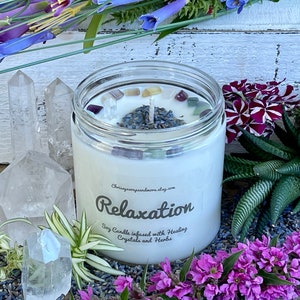 May include: A white soy candle with the text "Relaxation" and "Soy Candle infused with Healing Crystals and Herbs" on the label. The candle is surrounded by lavender, crystals, and flowers.