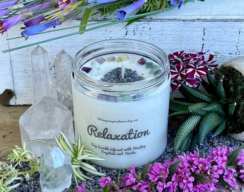 May include: A white soy candle with the text "Relaxation" and "Soy Candle infused with Healing Crystals and Herbs" on the label. The candle is surrounded by lavender, crystals, and flowers.
