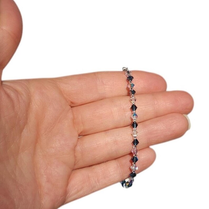 a beautiful navy blue blue and clear ab interspersed bicone crystal necklace upon a womans open palm against a white background.