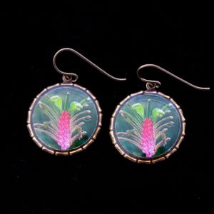 May include: A pair of gold-toned earrings with a green background and a pink flower design.