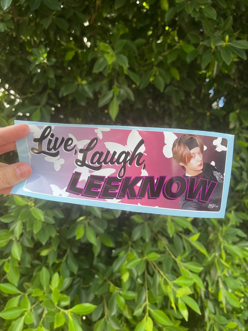 K&ouml;nnte beinhalten: Ein Aufkleber mit einem Schmetterlingsmuster in Pink, Blau und Wei&szlig;. Der Aufkleber zeigt den Text "Live, Laugh, LEEKNOW" in schwarzen und violetten Buchstaben. Im Hintergrund ist ein Foto einer Person mit braunen Haaren zu sehen, die eine schwarze Jacke und ein schwarzes Stirnband tr&auml;gt.