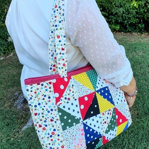 Pu&ograve; includere: Una borsa tote in patchwork con stampa floreale rosso, bianco e blu. La borsa ha una cerniera rosa e una tracolla lunga.