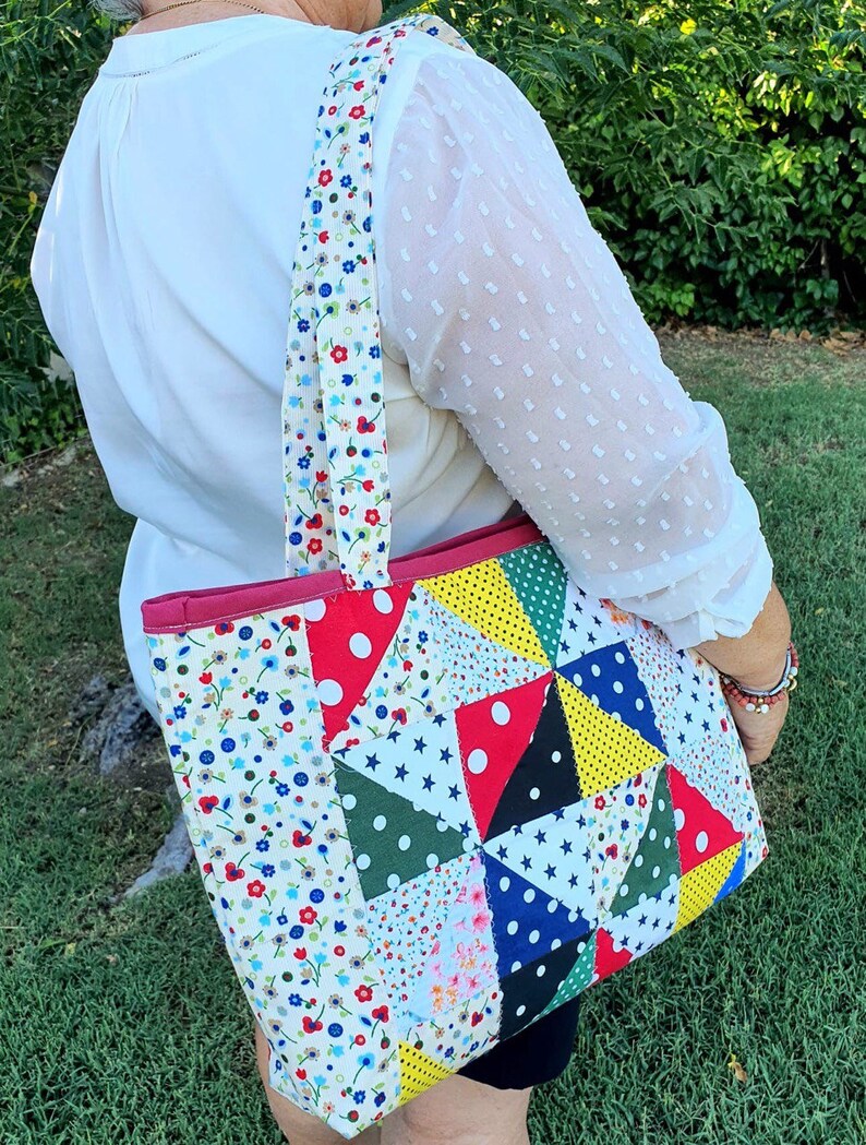 Pu&ograve; includere: Una borsa tote in patchwork con stampa floreale rosso, bianco e blu. La borsa ha una cerniera rosa e una tracolla lunga.