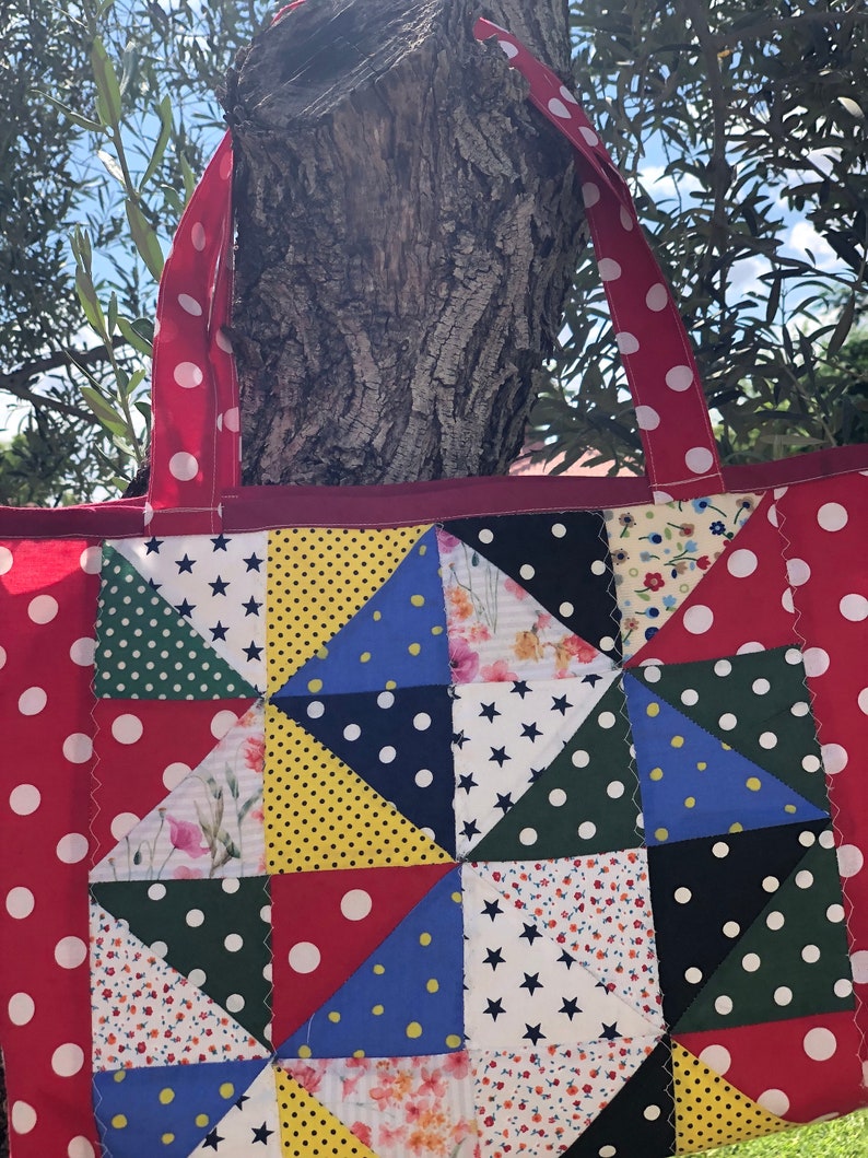 Pu&ograve; includere: Una borsa a tracolla rossa a pois bianchi con un design a patchwork che presenta vari tessuti con diversi motivi, tra cui stelle, pois e stampe floreali.