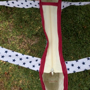 Pu&ograve; includere: Una borsa tote bianca con una cerniera rossa e stelle blu sulle maniglie. La borsa &egrave; foderata con un tessuto color crema.