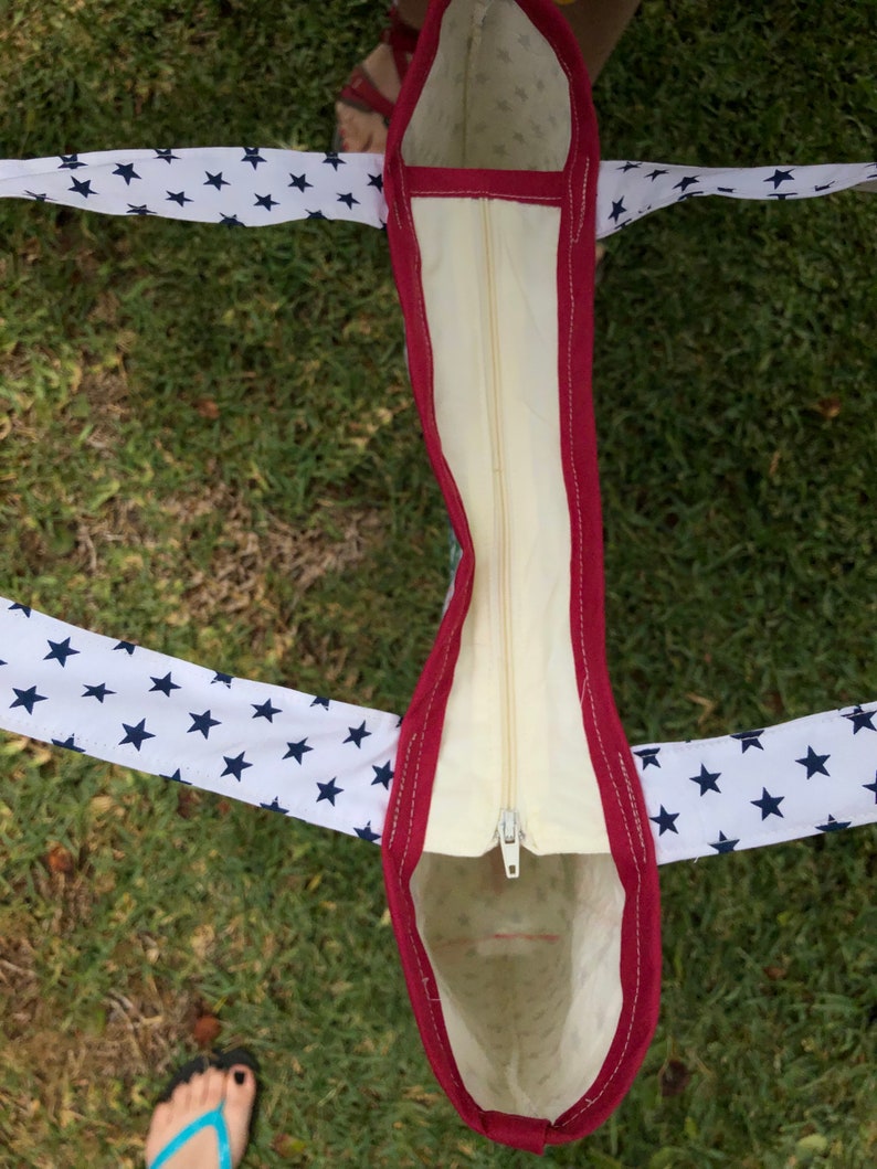 Pu&ograve; includere: Una borsa tote bianca con una cerniera rossa e stelle blu sulle maniglie. La borsa &egrave; foderata con un tessuto color crema.