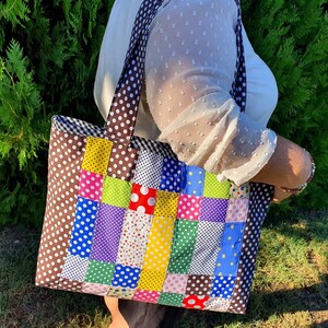 Pu&ograve; includere: Una borsa a mano in patchwork marrone e bianco con quadrati e pois colorati. La borsa ha un manico in tessuto marrone e una chiusura a zip.