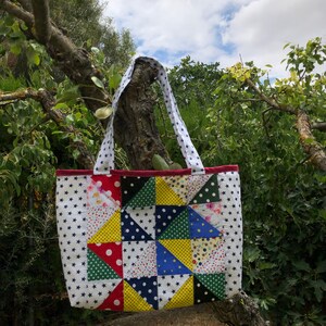 Pu&ograve; includere: Una borsa a tracolla in patchwork con sfondo bianco e motivi geometrici colorati in rosso, giallo, blu, verde e nero. La borsa ha due manici ed &egrave; realizzata in tessuto.