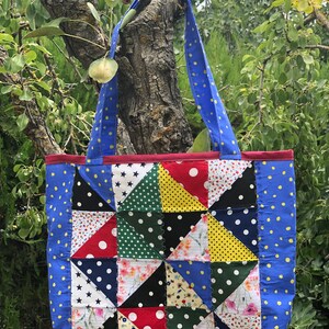 Pu&ograve; includere: Una borsa tote blu con un design a patchwork che presenta vari tessuti con pois, stelle e motivi floreali. La borsa ha due manici blu con pois gialli.