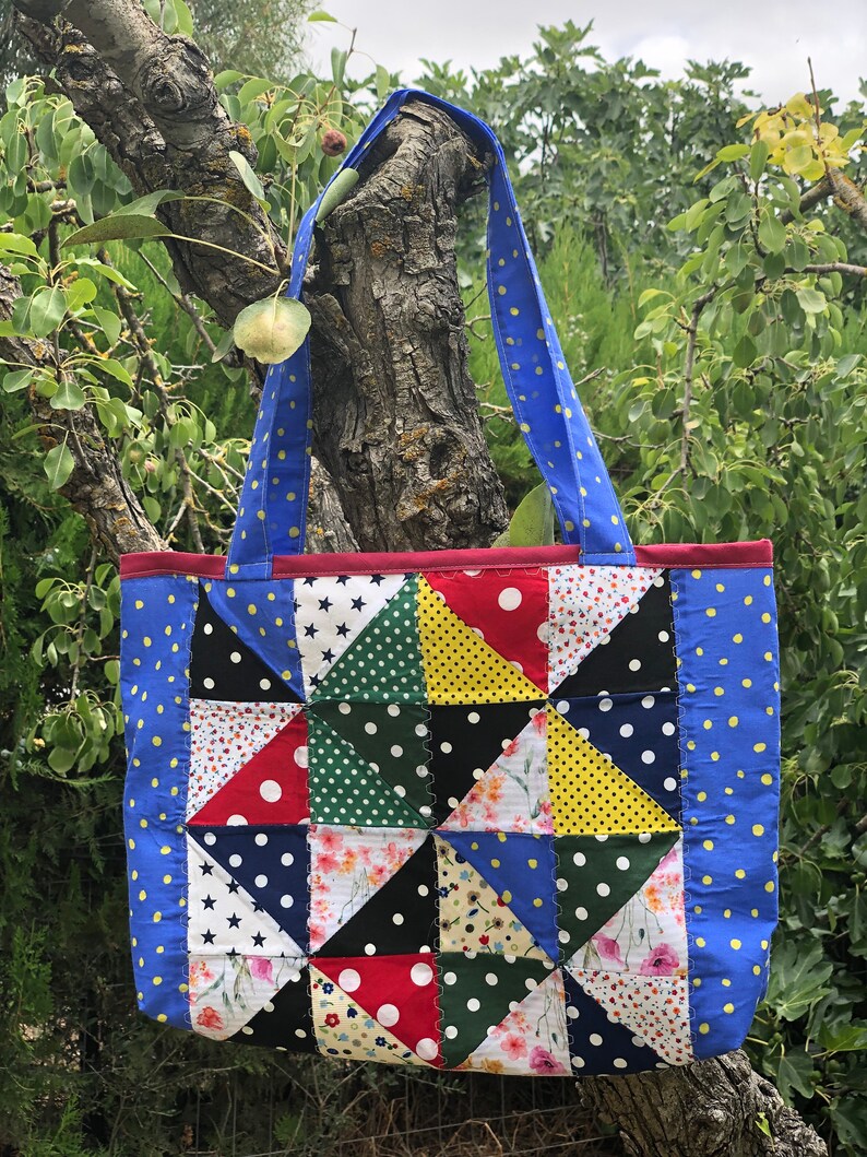 Pu&ograve; includere: Una borsa tote blu con un design a patchwork che presenta vari tessuti con pois, stelle e motivi floreali. La borsa ha due manici blu con pois gialli.