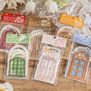 May include: A set of six sheets of decorative paper featuring vintage-style window designs. Each sheet has a different design, including a red window with a floral pattern, a green window with a floral pattern, a brown window with a floral pattern, a white window with a floral pattern, a blue window with a floral pattern, and a yellow window with a floral pattern. The sheets are labeled "Flower Garden Series" and have a number on each sheet.