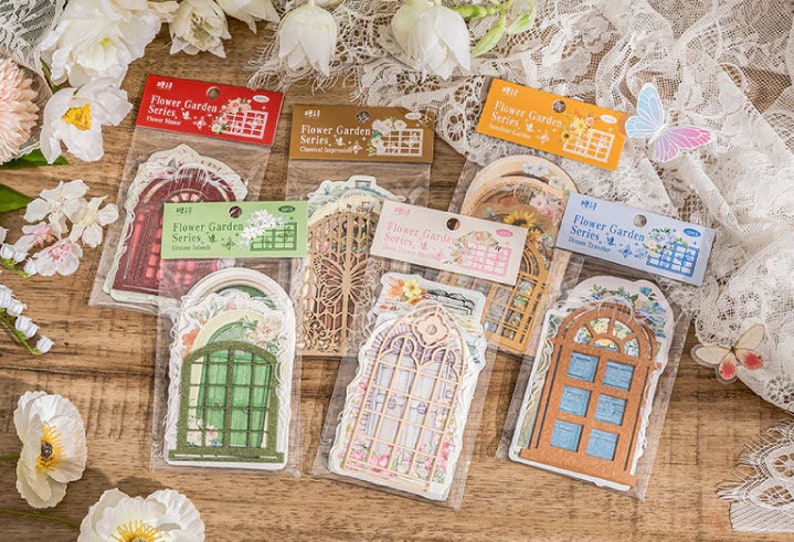 May include: A set of six sheets of decorative paper featuring vintage-style window designs. Each sheet has a different design, including a red window with a floral pattern, a green window with a floral pattern, a brown window with a floral pattern, a white window with a floral pattern, a blue window with a floral pattern, and a yellow window with a floral pattern. The sheets are labeled "Flower Garden Series" and have a number on each sheet.