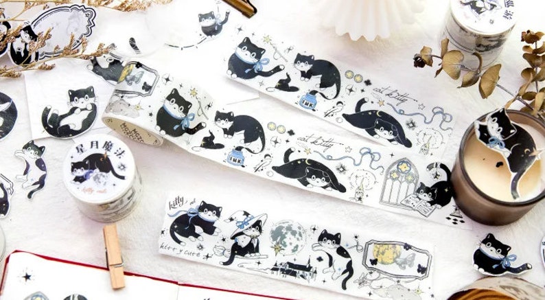 May include: Assortment of black and white washi tape rolls featuring a repeating pattern of cats, stars, and moons. The text on the tape reads "cat kitty" and "kitty and cat".