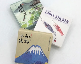 May include: Three small boxes of Japanese themed decorative stickers. The boxes are decorated with images of cranes, carp streamers, and Mount Fuji. The text on the boxes reads "LABEL STICKER", "信の恋人盒装贴纸/40 SHEET", and "拾光盒装贴纸/40SHEET".
