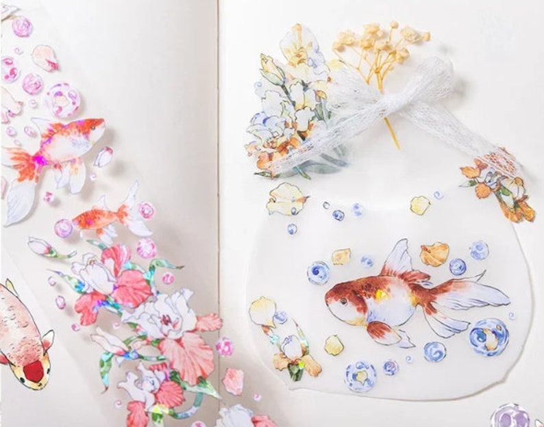 K&ouml;nnte beinhalten: Ein Blatt mit transparenten Aufklebern mit verschiedenen bunten Illustrationen. Die Aufkleber zeigen Goldfische, Blumen und Blasen. Die Aufkleber sind perfekt, um Tageb&uuml;chern, Planern und anderen Bastelprojekten einen Hauch von Verspieltheit zu verleihen.