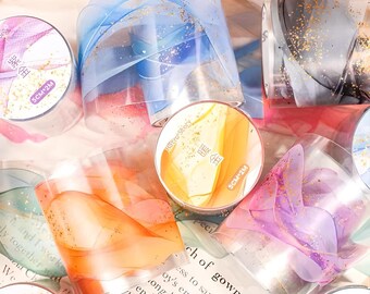 May include: Assortment of decorative washi tapes with gold glitter and abstract designs in blue, orange, purple, and black. The tapes are packaged in clear plastic containers with labels that read "SCM-2M" and "暖金".