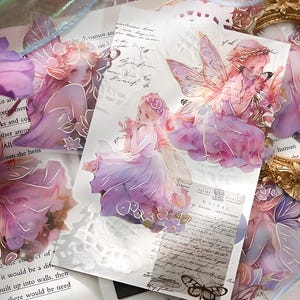 May include: A set of four transparent, purple and pink fairy stickers with delicate wings and floral details. The stickers are printed on a white background and are perfect for adding a touch of whimsy to journals, planners, or other craft projects.