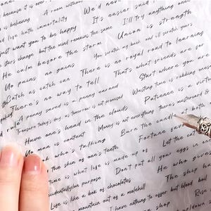 May include: A close-up of a handwritten note on a white background with a silver pen. The note contains inspirational quotes and sayings about life, happiness, and success. The text includes phrases like "Seeing is believing", "There is no royal road to learning", and "Patience is a virtue".
