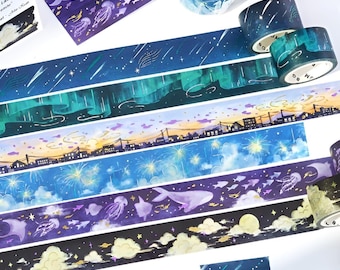 May include: Decorative washi tape rolls featuring various celestial and aquatic designs. The tapes showcase illustrations of shooting stars, northern lights, cityscapes, fireworks, whales, jellyfish, and clouds. The color palette includes blues, purples, and yellows.