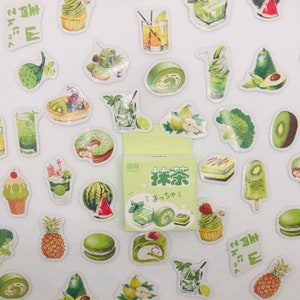 May include: A sheet of stickers featuring various green-themed designs, including matcha drinks, desserts, fruits, and vegetables. The stickers are printed on white paper and have a glossy finish. The sheet also includes the text "抹茶" in Japanese, which means "matcha".