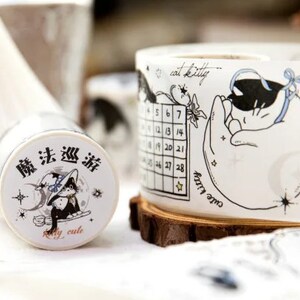 May include: Two rolls of decorative washi tape with black and white illustrations. One roll features a cat sleeping on a crescent moon with stars and the text "one cat kitty". The other roll features a cat wearing a witch's hat with the text "魔法 巡游" and "really cute".