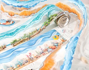 May include: Decorative washi tape featuring a beach scene with blue ocean waves, sand, and seashells. The tape roll has the text "have a good day". A small boat and a yellow inflatable ring are also visible.