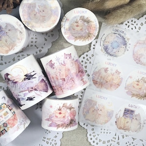 May include: Assortment of washi tape rolls with various pastel-colored illustrations of cats, birds, and other animals. The tape is labeled "Lucky" and features a whimsical, vintage aesthetic.