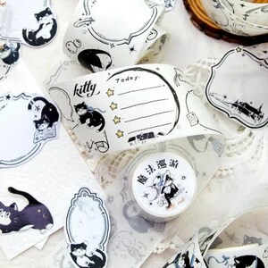 May include: Assortment of decorative washi tapes featuring black and white illustrations of cats, stars, and moons. The tapes are on a white background with a lace overlay. The text "kitty" and "Today" are visible on one of the tapes.