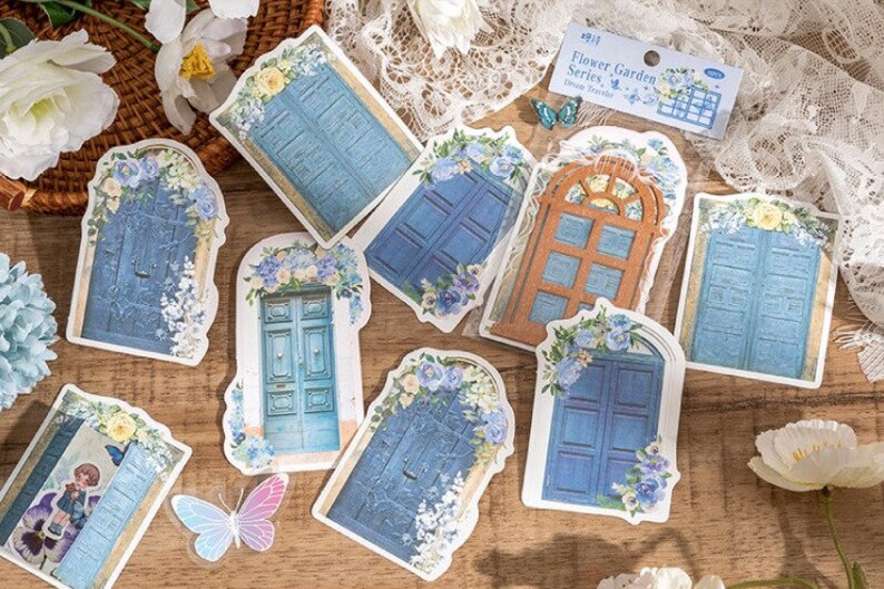 May include: A set of nine decorative stickers featuring blue and brown doors with floral accents. The stickers are part of a "Flower Garden Series" and are designed for use in a traveler's journal.