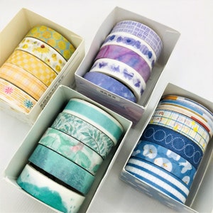 May include: Five boxes of colorful washi tape rolls. Each box contains different patterns and colors of washi tape. The washi tape is a popular craft supply used for decorating journals, planners, and other paper crafts.