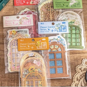 May include: A set of decorative window stickers in a clear plastic bag. The stickers are printed with a floral design and have a vintage aesthetic. The stickers are labeled "Flower Garden Series" with different sub-series names like "Sunshine Garden", "Dream Traveler", "Moon Flower Shade", "Distant Islands", and "Flower Manor".