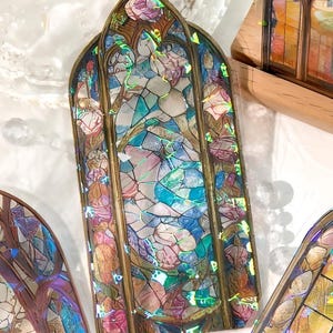 May include: Decorative stained glass window stickers with a cathedral arch design. The stickers feature a colorful mosaic of blues, pinks, and greens, framed by a gold-colored border. The design evokes a vintage aesthetic.