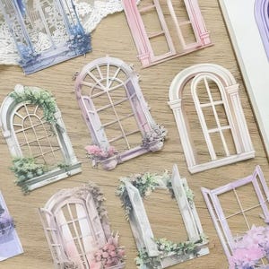 Pode incluir: Um conjunto de 11 adesivos decorativos para janelas com detalhes florais e de folhagem. Os adesivos são de várias cores pastel e apresentam diferentes designs de janelas, incluindo formas arqueadas e retangulares.