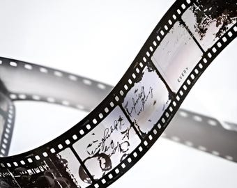 Może przedstawiać: Pasek czarno-białej taśmy filmowej z widocznymi klatkami, zawierający odręczny skrypt i abstrakcyjne obrazy. Taśma jest zakrzywiona, z częścią cienia widoczną na białym tle. Słowo "EVERY" jest widoczne na jednej z klatek.