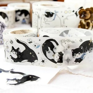 May include: A roll of clear washi tape with black and white illustrations of cats, stars, and clouds. The tape is labeled "猫 小 猫" in Japanese characters.