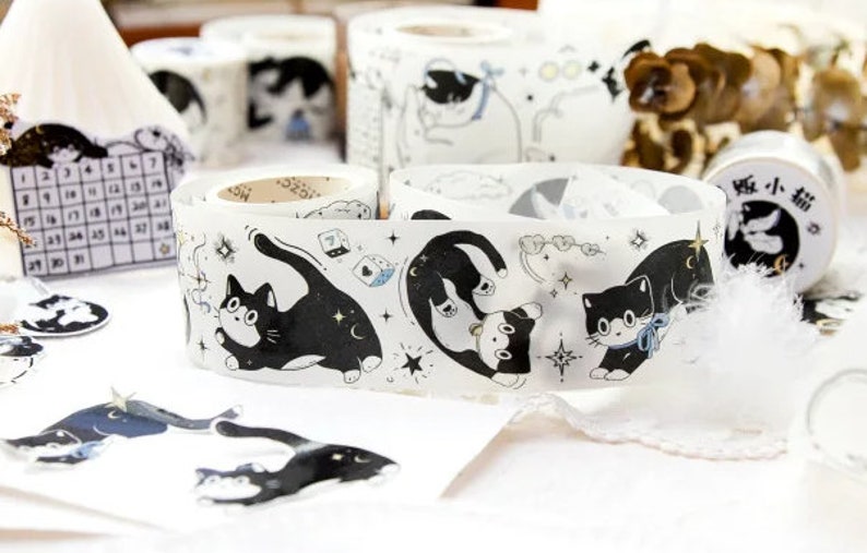May include: A roll of clear washi tape with black and white illustrations of cats, stars, and clouds. The tape is labeled "猫 小 猫" in Japanese characters.