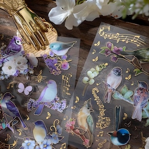 2 vellen, verguld, bladgoud, glanzend, PET-stickers. VOGELS. Muzieknoten. Bloemen
