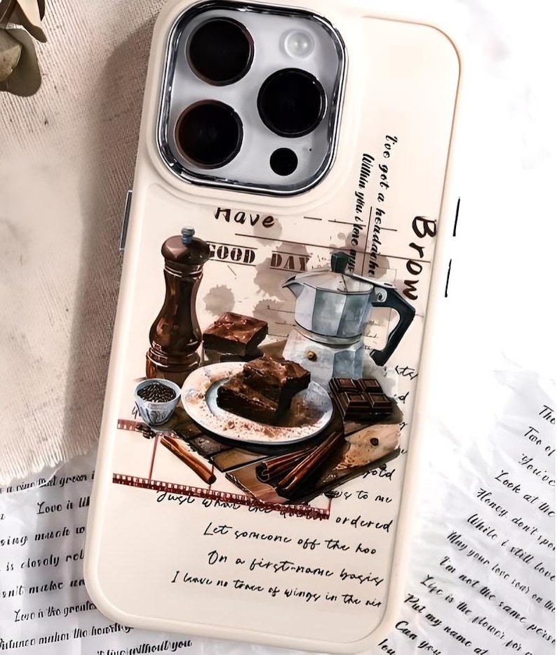 May include: A white phone case with a watercolor design of a coffee pot, chocolate squares, and a plate of brownies. The text "Have a Good Day" is written on the case.