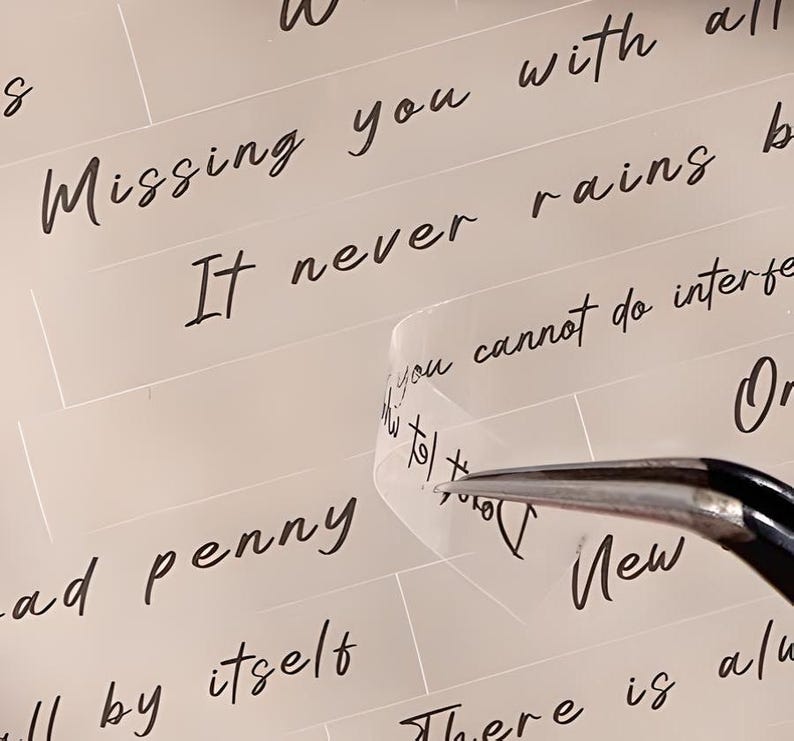 May include: A close-up of a clear sticker with the text "It never rains but it pours" written in black ink. The sticker is being peeled off of a white surface with the text "Missing you with all" and "ad penny" visible.