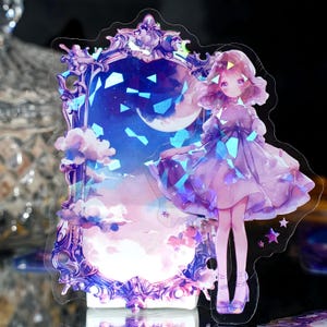 Puede incluir: Una pegatina holográfica con una niña con un vestido morado de pie frente a un espejo con una luna creciente y estrellas en el reflejo. El espejo tiene un marco adornado.