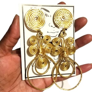 May include: A pair of gold wire earrings with a spiral design. The earrings are large and dangle. The spirals are white with gold wire wrapped around them.