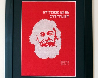 May include: A framed red cross-stitch artwork depicting a white portrait of Karl Marx with the text "Stitched up by Capitalism" and the signature "leond 2011".