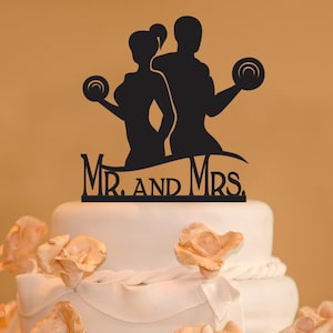 May include: Black silhouette of a couple lifting weights, with the text "Mr. and Mrs." below. This is a wedding cake topper.