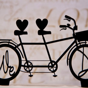 May include: Black silhouette of a tandem bicycle with two heart-shaped seats and the word "We" inscribed on the front tire.