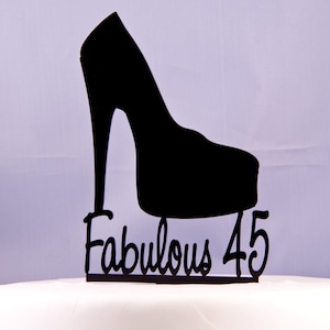 May include: Black silhouette cake topper featuring a high-heeled shoe design. The text "Fabulous 45" is displayed below the shoe. This decorative topper is suitable for a birthday celebration.