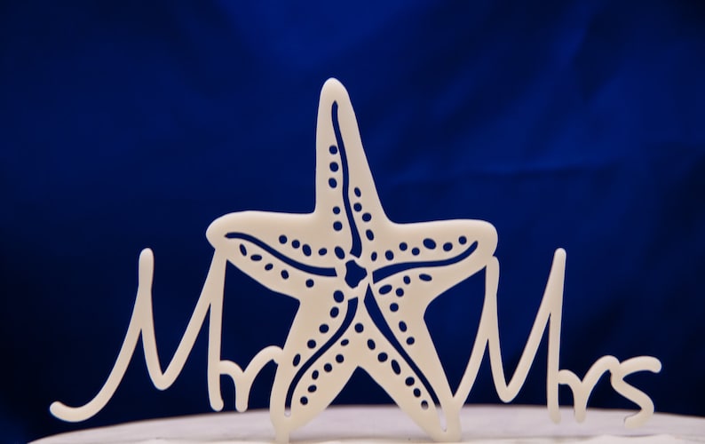 May include: White cake topper with a starfish design and the words "Mr & Mrs" in cursive.