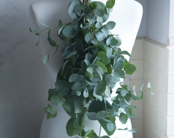 May include: A white dress form with a bunch of eucalyptus leaves tied around the neck.