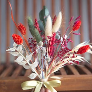 May include: A small bouquet of dried flowers tied with a green ribbon. The bouquet includes red, white, and green flowers.
